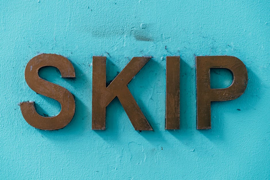Close-up of large, three-dimensional brown metal letters spelling 'SKIP' mounted on a bright turquoise wall, with visible textures and slight imperfections. The letters are arranged in a straight line, with the 'S' on the left, followed by 'K', 'I', and 'P'. The wall has a slightly rough surface, and the lighting creates minimal shadows around the edges of the letters. This image appears to be taken outdoors or in a well-lit interior space during daylight. The display of the word 'SKIP' may relate to waste disposal or skip hire services, relevant in the context of house removals or home relocation, as provided by Man with Van Petersham, which offers comprehensive moving and furniture transport solutions.